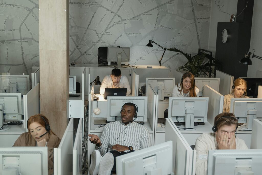 pexels-photo-5453859-5453859 A group of diverse call center employees working with computers and headsets in cubicles.